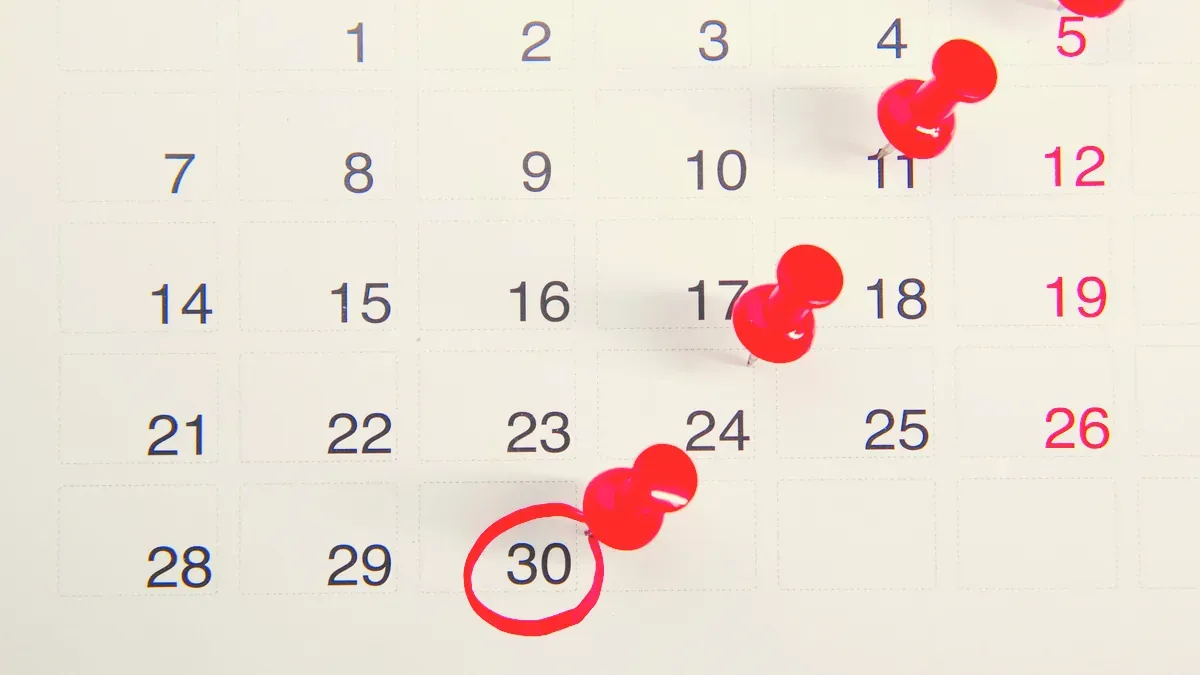 Väggkalender med röda kartnålar och en röd ring runt den trettionde